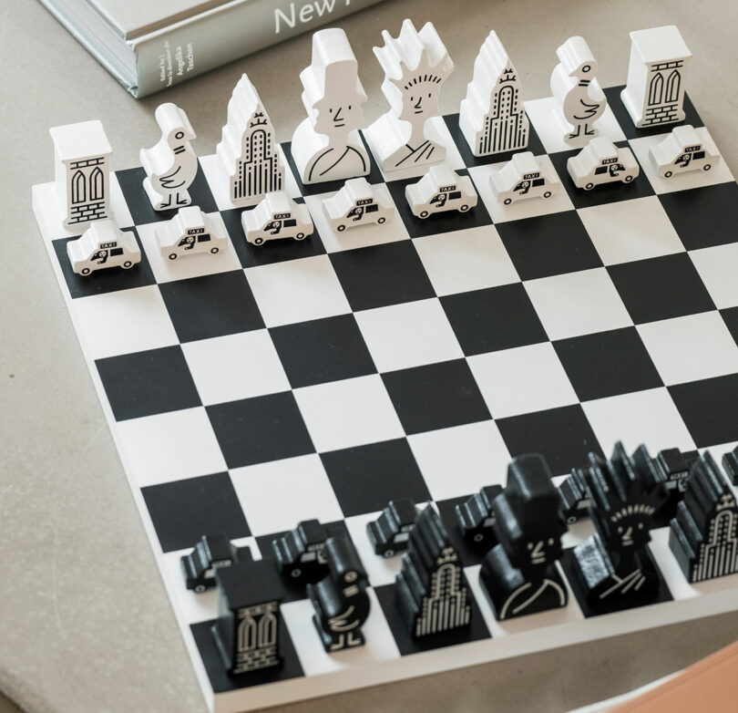This Chess Printworks set showcases a black and white theme with uniquely designed pieces, featuring abstract figures and buildings, elegantly displayed on the chessboard.