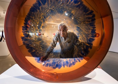A man smiling as seen through an semi-transparent orange disk with inky blue patterning.
