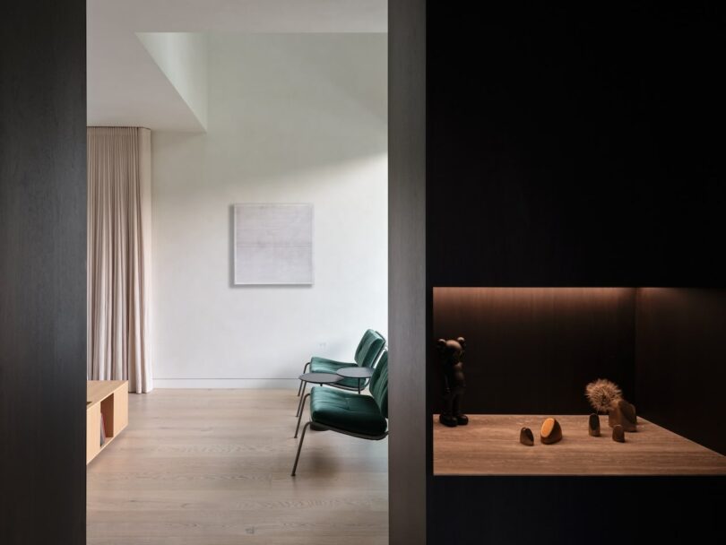 Minimalist interior with two green chairs facing a beige wall and a brown alcove displaying decorative items. Neutral tones and wooden flooring create a modern, serene ambiance.