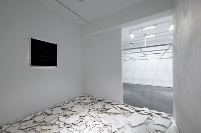View of a gallery with several pieces of drywall on the floor and a screen on the wall.
