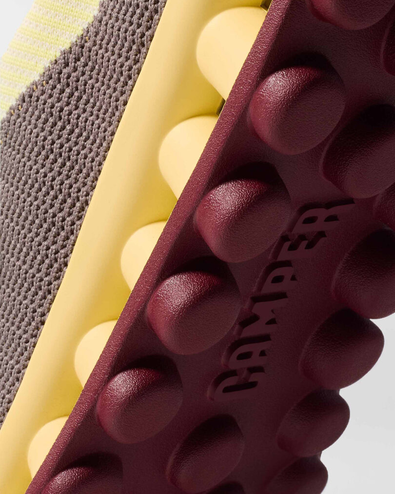 Close-up of a shoe, showing a textured brown fabric upper and a bumpy sole with the word 