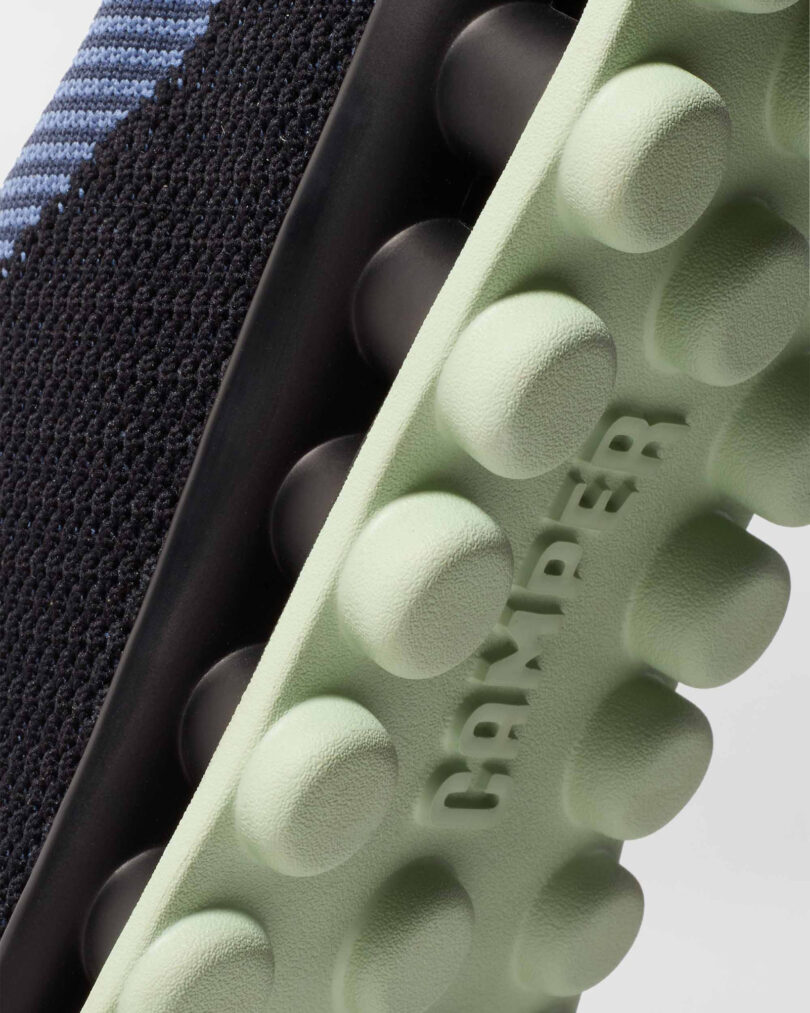 Close-up of a black sneaker with a textured green sole featuring round protrusions and the word 