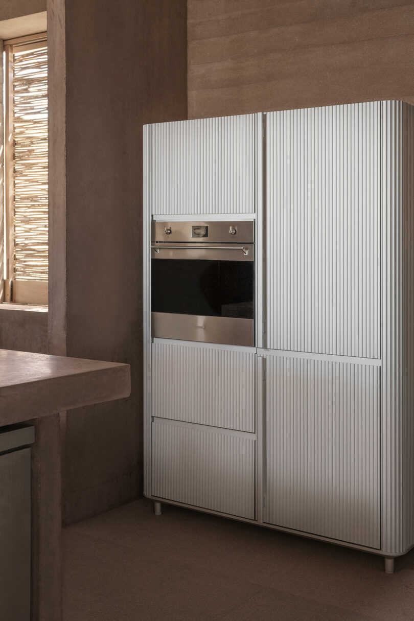 A modern kitchen with light-colored cabinetry and a built-in oven, featuring a rustic window with wooden slats.