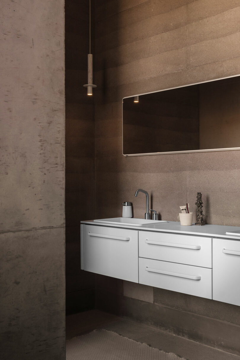 Modern bathroom with textured walls, a white floating vanity with two drawers, a sleek faucet, a large horizontal mirror, a ceiling light, and minimal decor items.