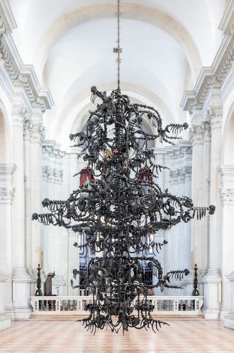 Intricate black metal sculpture with organic shapes hanging in a bright, arched white interior.