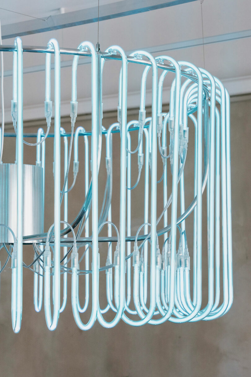 A modern, geometric chandelier with tubular neon lights arranged in a circular pattern, emitting a cool blue glow, hangs from the ceiling.