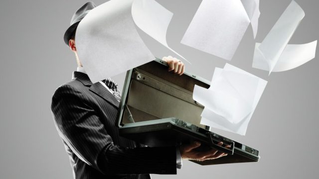 CEO-of-AI-ad-tech-firm-pledging-world-free-of-fraud.jpg Man in dark pinstripe suit holding open a briefcase, from which papers are flying out and covering his face.