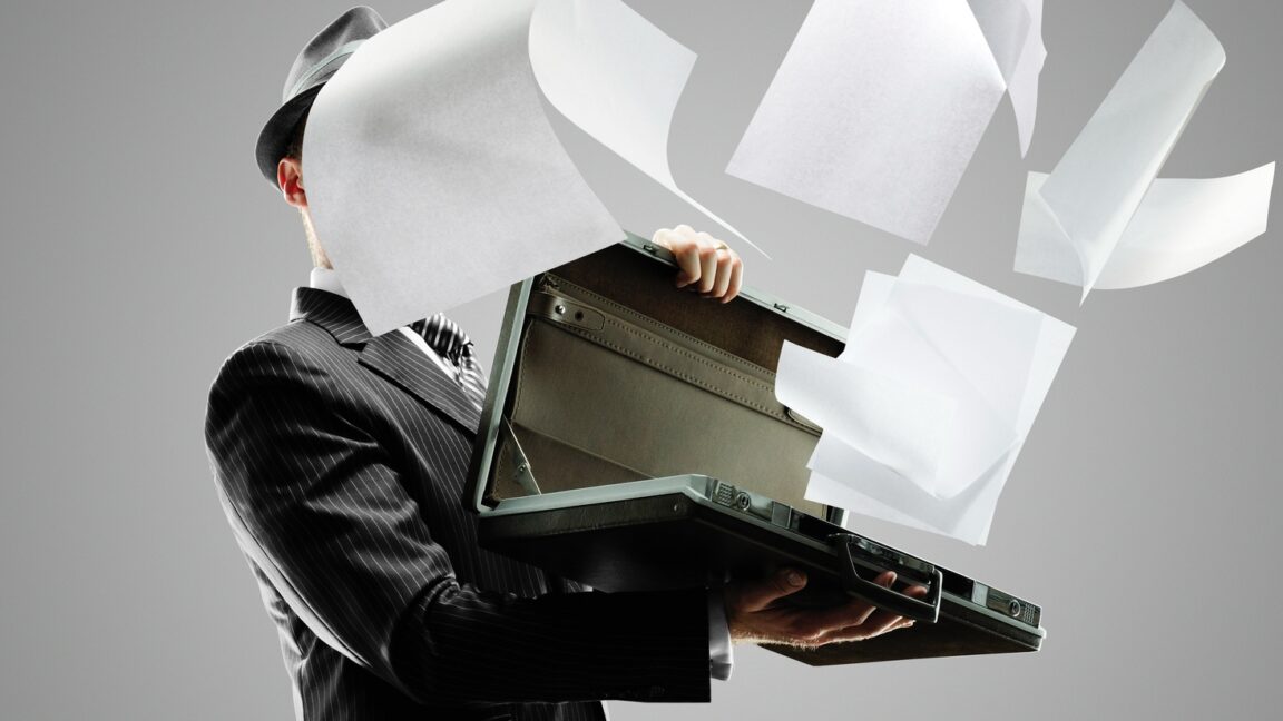 CEO-of-AI-ad-tech-firm-pledging-world-free-of-fraud.jpg Man in dark pinstripe suit holding open a briefcase, from which papers are flying out and covering his face.