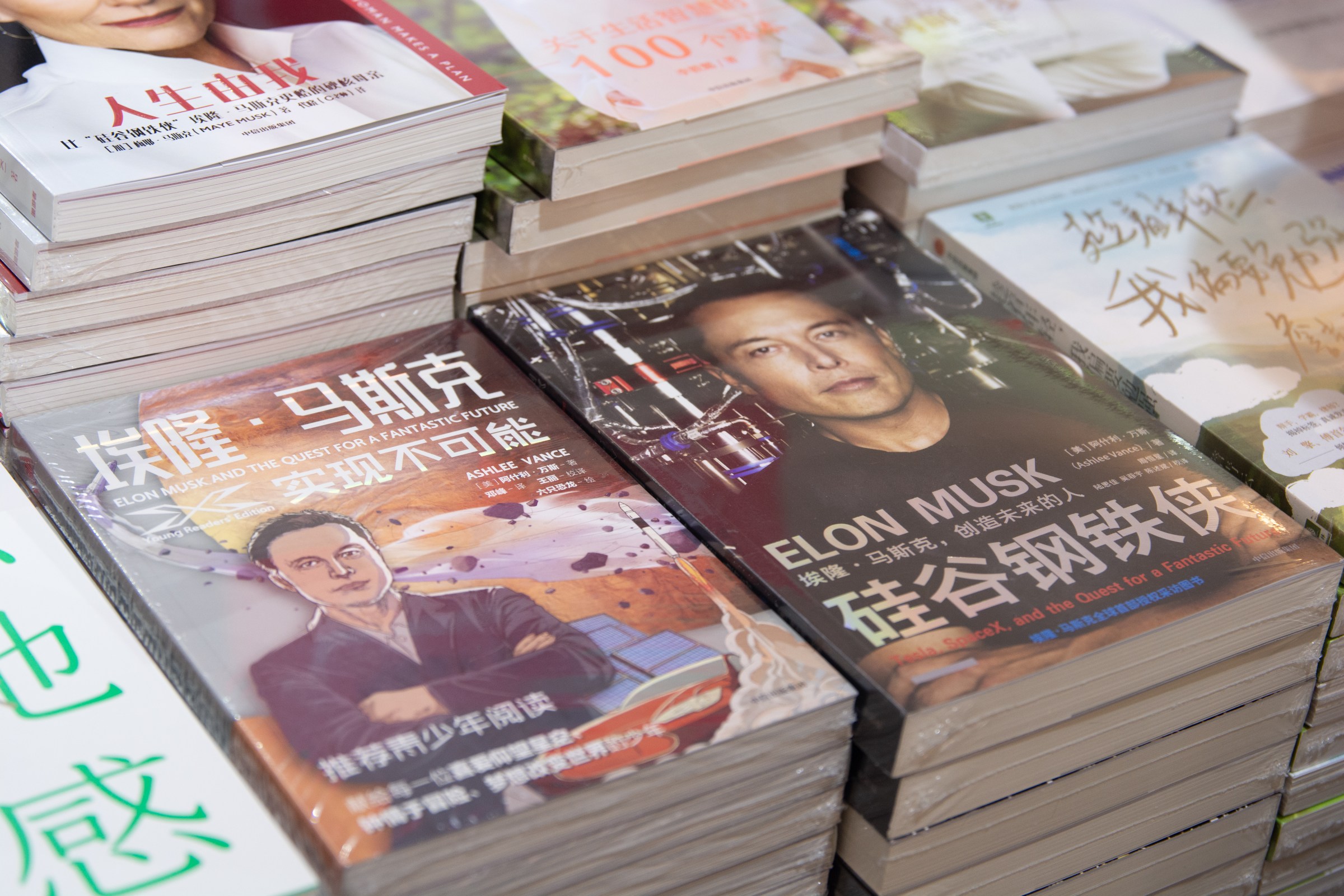 Elon-Musk-and-China-Could-Teslas-bottom-line-influence-Trumps.jpg Stacks of books in Chinese with Elon Musk on the cover are piled on a table.