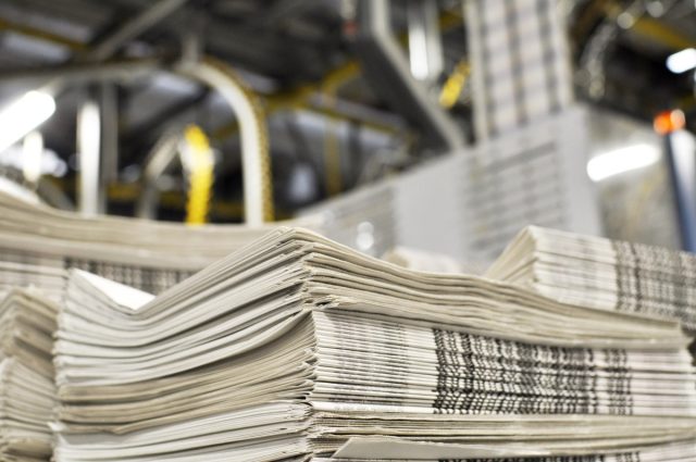 Lee-Enterprises-ransomware-attack-hits-freelance-and-contractor-payments.jpg stack of freshly printed daily newspapers transported to a printing plant, in the background machines and technical equipment of a large printing plant