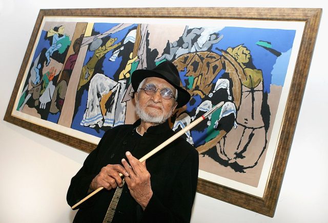 A man with a white beard in front of a painting.