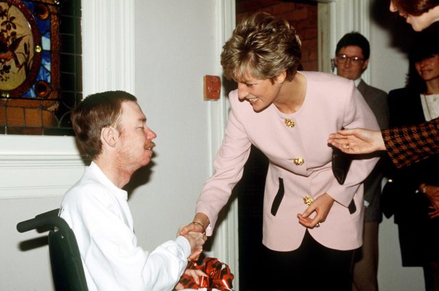 Meghan-Markles-new-Netflix-show-With-Love-Meghan-is-bland.jpeg Diana, in a pink and black jacketed suit, shakes hands with a frail man in a wheelchair, while other people stand behind her.
