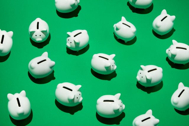 Next-Insurance-gets-scooped-up-by-Munich-Re-for-26B.jpg 16 small white piggy banks placed randomly on green surface, high angle of view