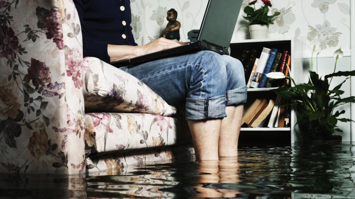 Open-Source-devs-say-AI-crawlers-dominate-traffic-forcing-blocks.jpg man sitting in sofa in a flooded living room, feets in water, writing on a laptop