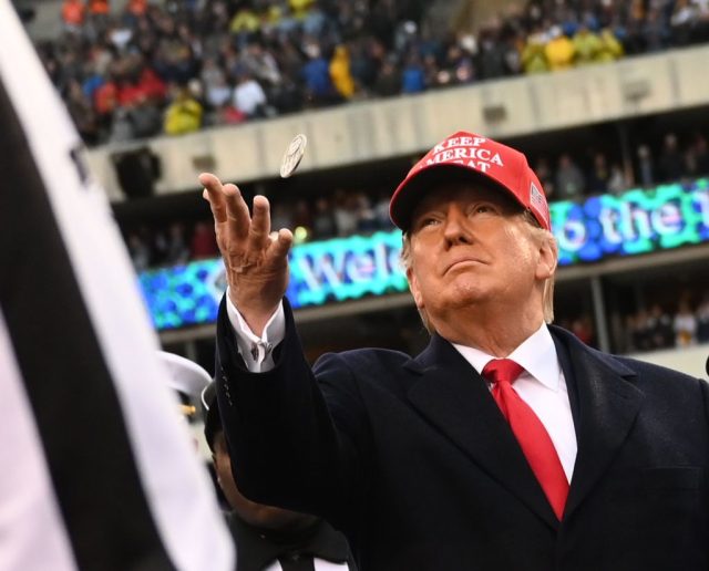 Trump-supporters-lose-billion-as-TRUMPs-value-falls-of-a.jpg A man in a suit and a red hat tosses a coin at a stadium.
