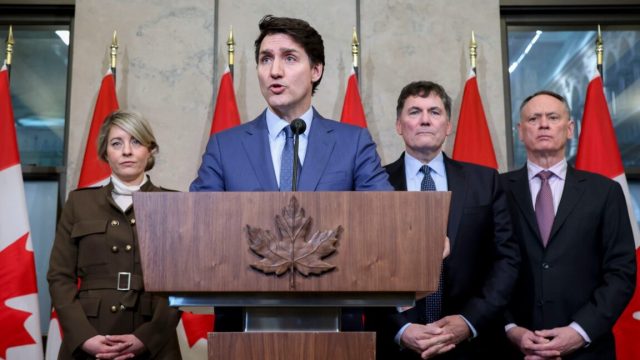 Trumps-25-tariffs-take-effect-Canadian-PM-calls-it-a.jpg Canadian Prime Minister Justin Trudeau speaks at a podium during a news conference, with other government officials standing behind him.
