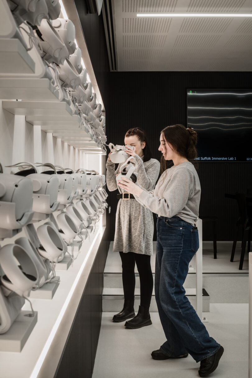 Two people interact with virtual reality headsets in a modern, well-lit room with a wall display of numerous headsets.