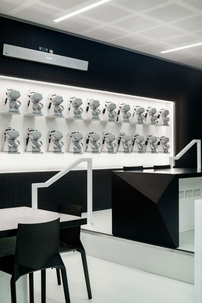 Modern interior by WindsorPatania Architects, featuring a wall display of mounted gray devices, a sleek black table and chairs, and a geometric black and white counter.