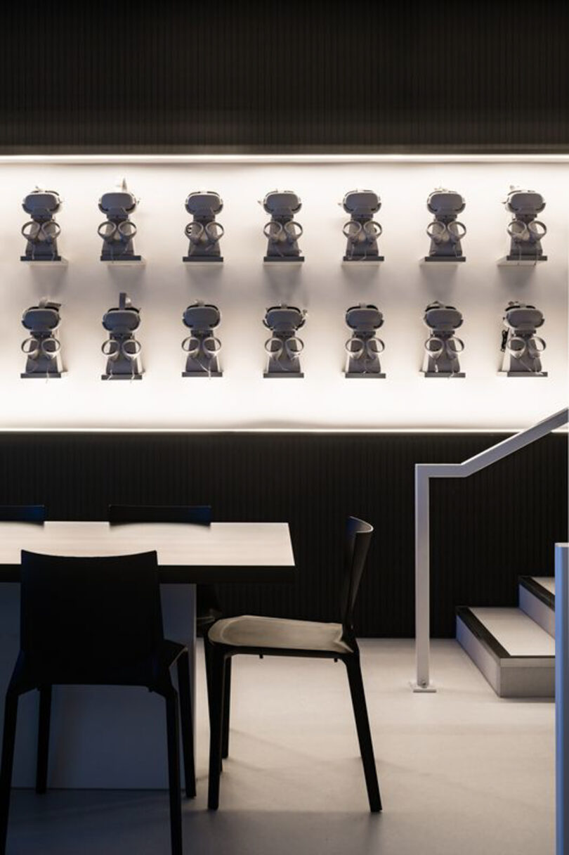 A wall displays multiple small robot figures in a modern interior. A table and chairs are in the foreground.