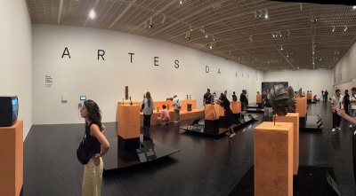 View of a museum exhibition showing traditional African art works. Various people view them. 