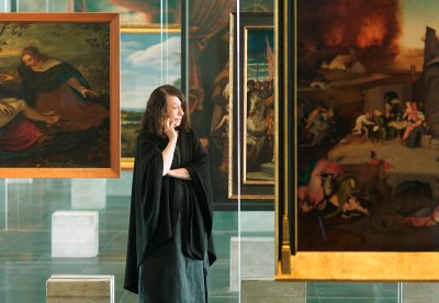 A woman stands among MASP's iconic Lisa Bo Bardi–designed glass easels with Old Master paintings hanging on them. 