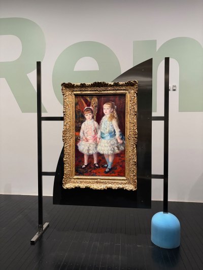 View of a Renoir painting on a metal easel with other elements. 