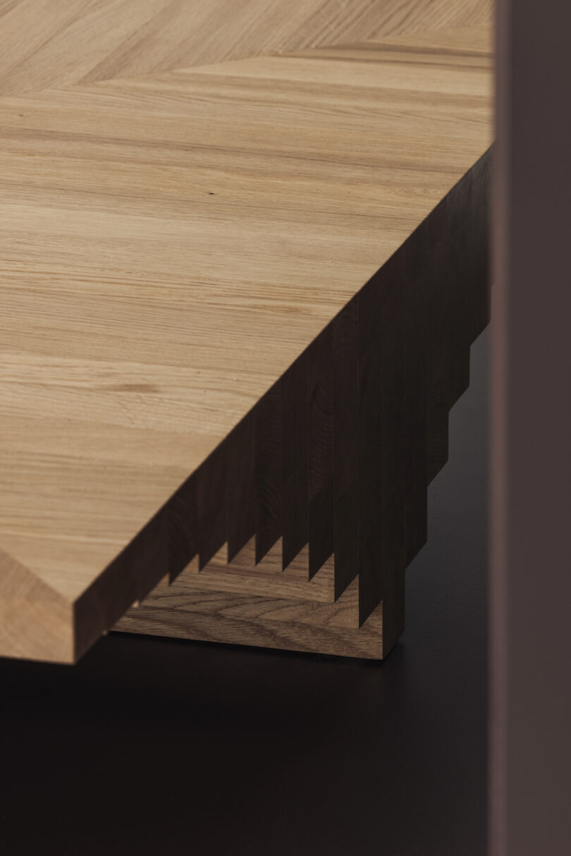 Close-up of a wooden table corner with a unique zigzagged edge, resting on a dark surface