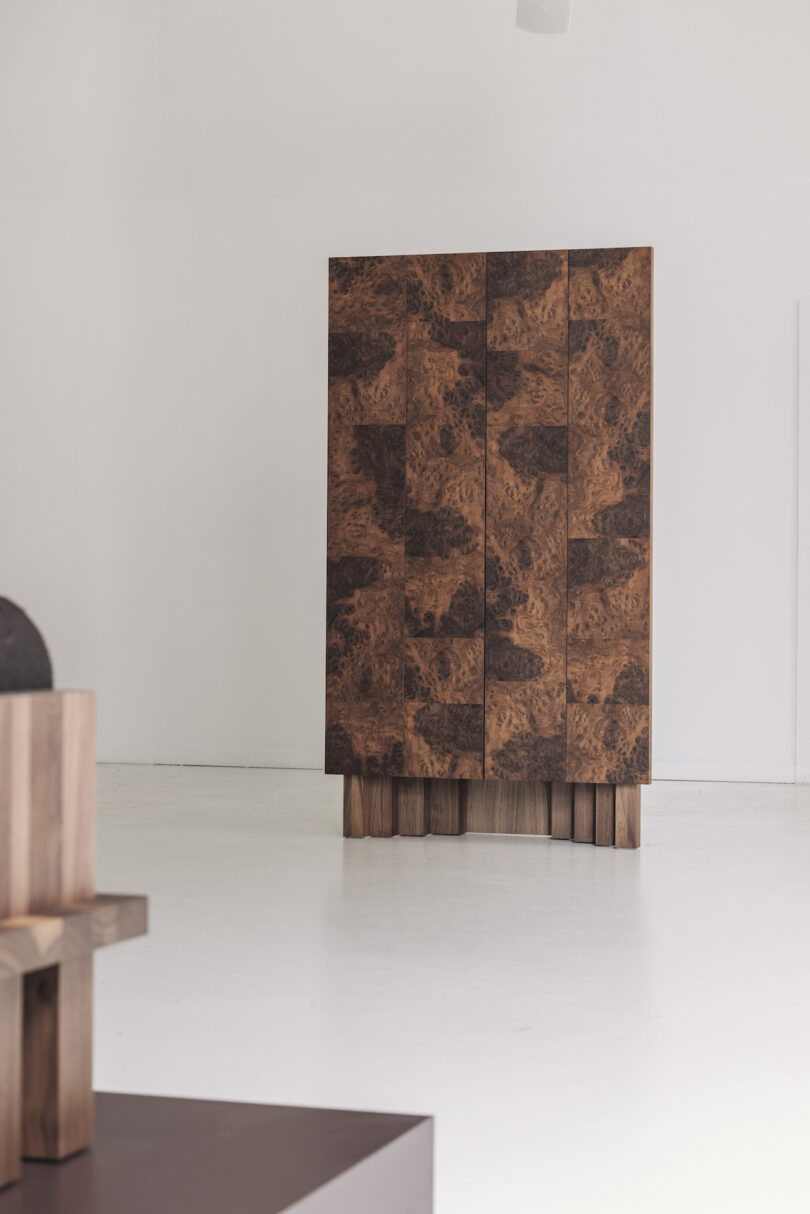 Wooden cabinet with a textured, brown pattern stands in a minimalistic, white room
