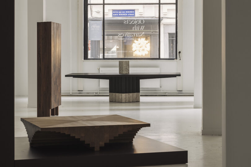 Modern gallery interior with geometric wooden sculptures and large windows. Light fills the space, highlighting the contemporary design