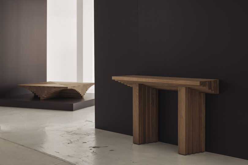 Wooden console table and geometric coffee table in a minimalist interior with dark walls and a concrete floor