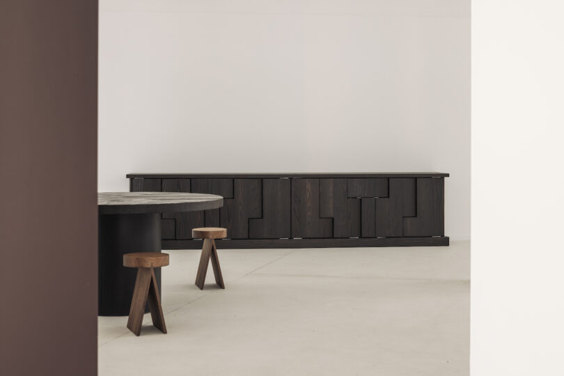 A minimalist stone console table with vertical grooves stands against a plain white wall and light-colored floor