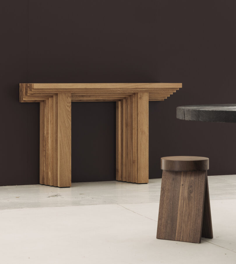 Wooden console table against a dark wall with a wooden stool on a light floor