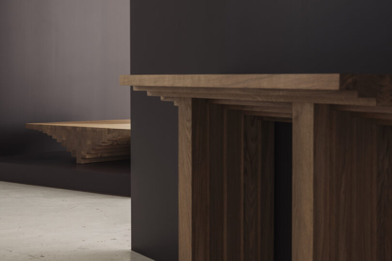Modern wood table with geometric design placed against a dark wall, featuring layered edges and a polished surface