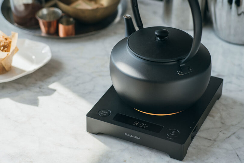 A black kettle is placed on an electric hot plate displaying 93°C, on a marble countertop.