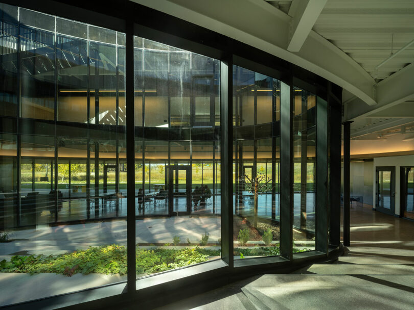 The interior view of this modern building, a stunning creation by CLB Architects, features large windows that beautifully reflect the lush green outdoors while flooding the space with natural light.