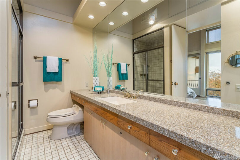 Bathroom with a large granite countertop, dual sinks, and big mirror. The room features a shower with sliding doors and teal towels.