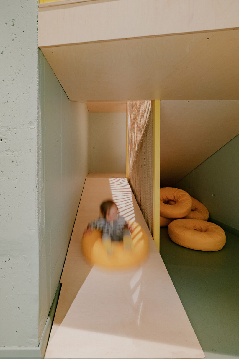 Child sliding down a play area slide on a yellow circular cushion, heading towards similar cushions at the bottom.