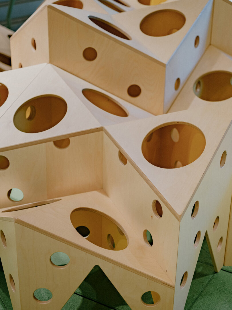 Wooden geometric blocks with circular cutouts stacked in an abstract formation on a green surface.
