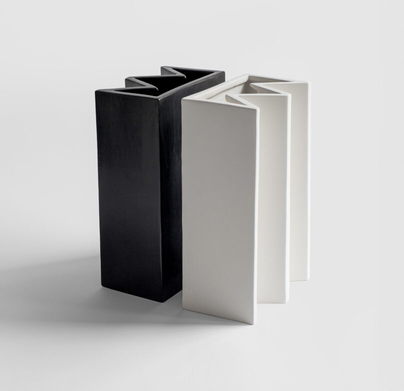 Two interlocking geometric sculptures, one black and one white, with rectangular and angular forms, set against a plain white background.