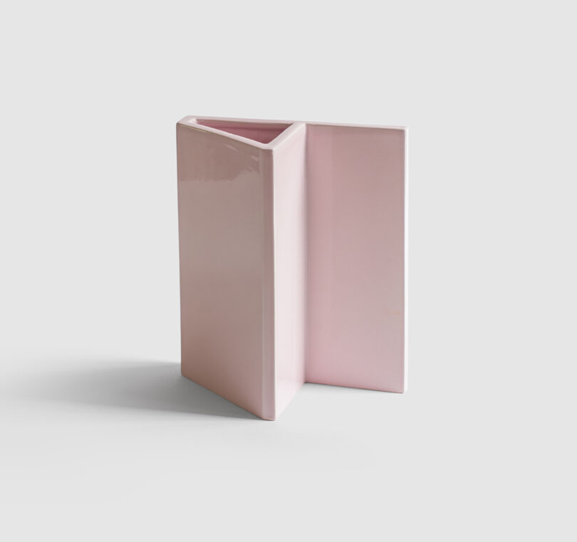 A geometric, pale pink ceramic vase with a modern, angular design set against a plain white background.