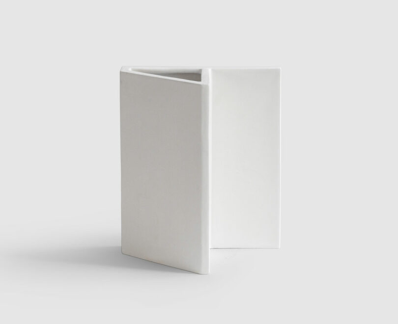 A minimalist Kish O Mat white ceramic vase with a triangular shape, featuring clean, straight lines on a light gray background.