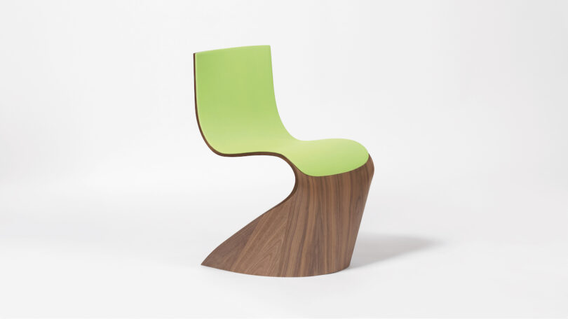 Curved, modern chair with a green seat and wooden base, set against a plain white background