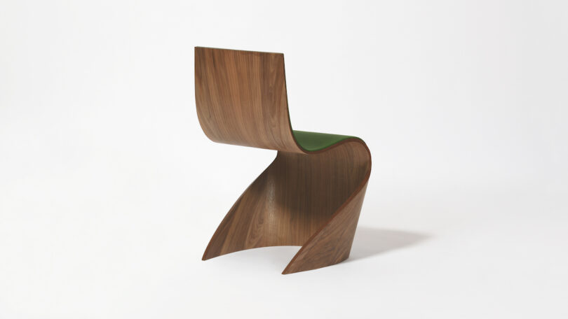 Curved, modern chair with a green seat and wooden base, set against a plain white background