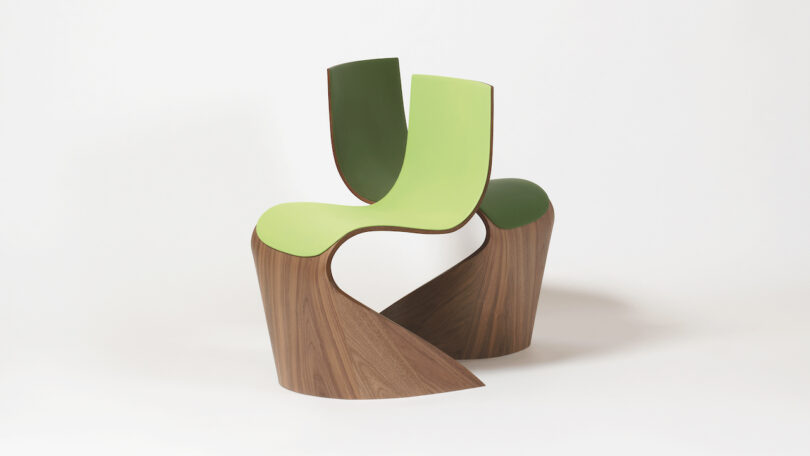 A modern chair with a twisted wooden base and a green, curved seat and backrest