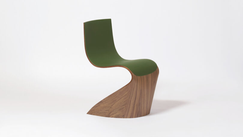 Curved, modern chair with a green seat and wooden base, set against a plain white background