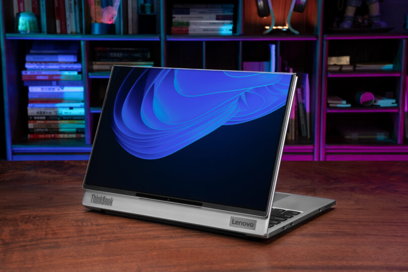 The Lenovo ThinkBook Flip laptop, with its vibrant blue screen, sits elegantly on a wooden table. Behind it, a bookshelf adorned with colorful lights adds a touch of whimsy to the scene.