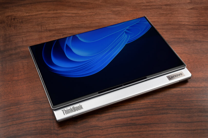 A closed Lenovo ThinkBook Flip rests on a wooden surface, its screen displaying a vibrant blue abstract design.