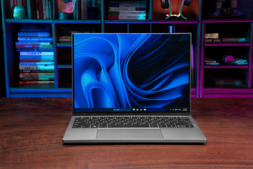 A ThinkBook Flip laptop, displaying a blue abstract wallpaper, sits elegantly on a wooden desk, framed by vibrant bookshelves in the background.