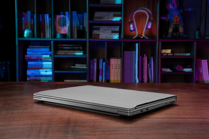 A ThinkBook Flip rests closed on a wooden table, surrounded by colorful books and lighted shelves that add a vibrant touch to the scene.