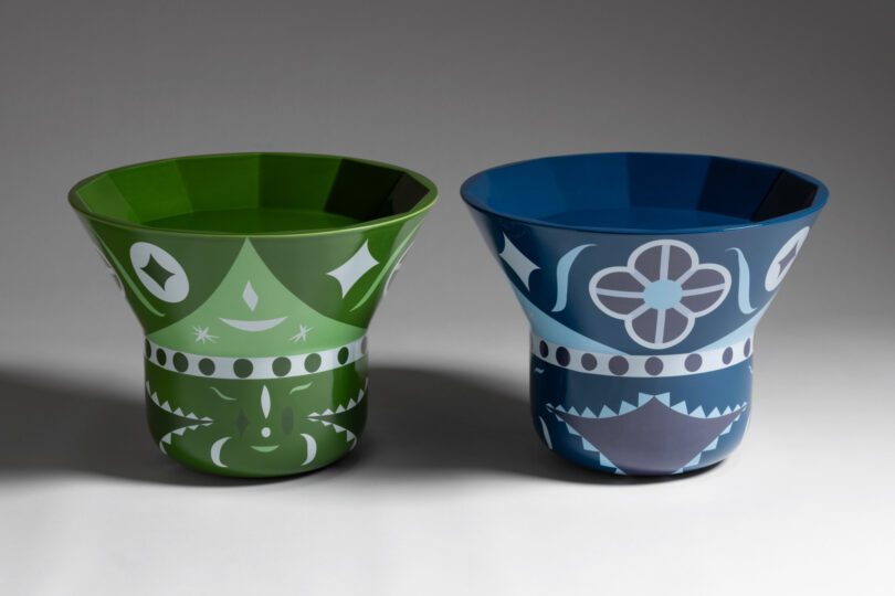 Two decorative, flared pots with geometric patterns. One is green, the other blue, both featuring white and gray designs.